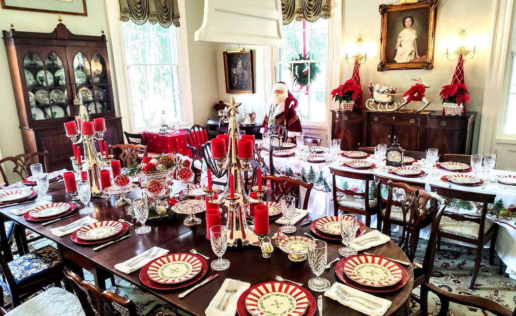 Large dining room with two large dark wooden tables filled with Christmas decorations and placesettings